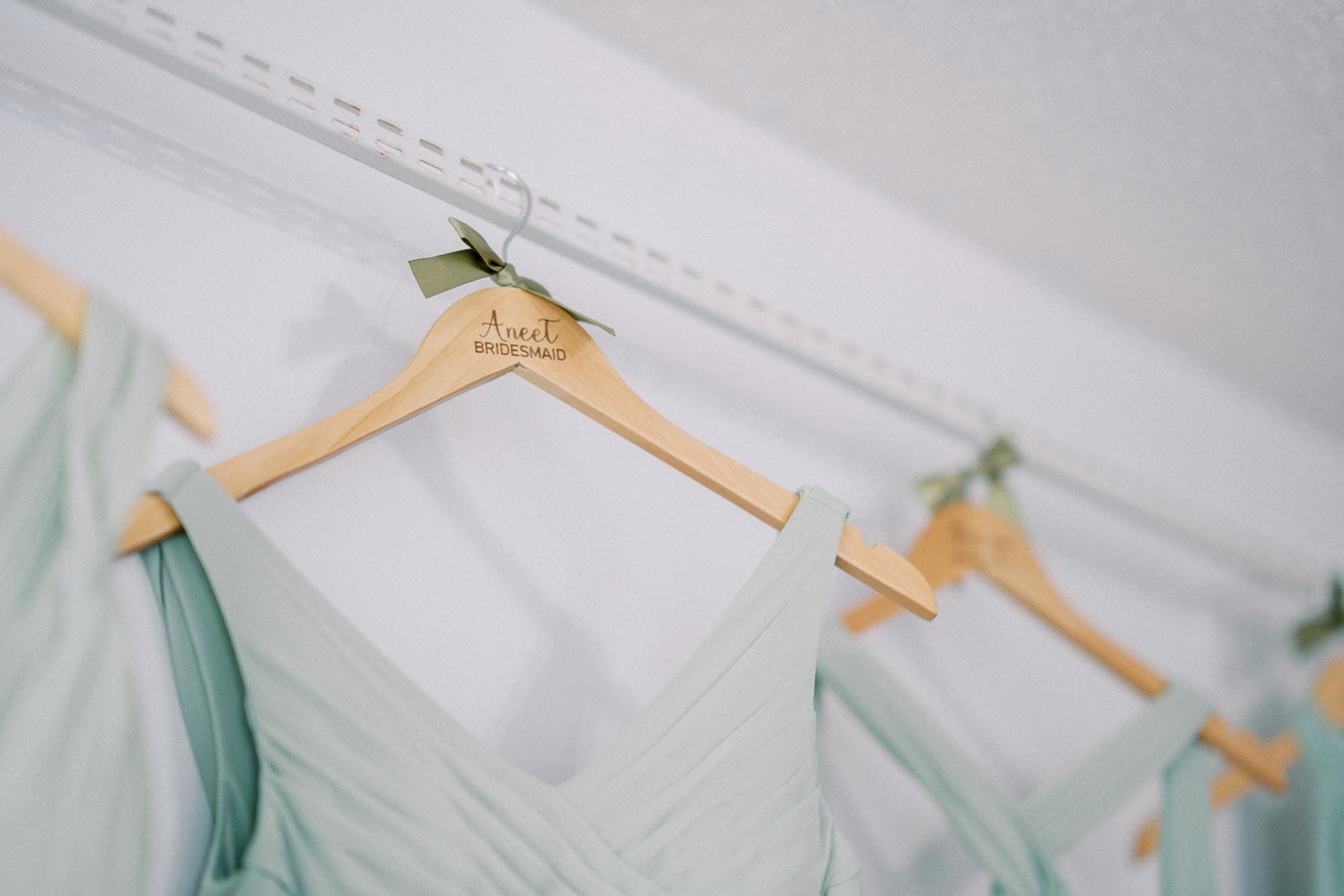 Light blue bridesmaid dresses hanging neatly on personalized wooden hangers with green bows.