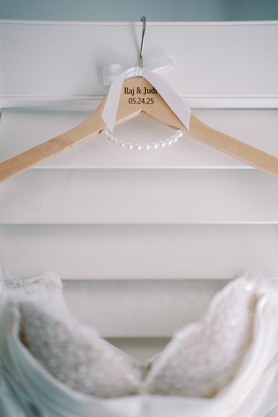 Wedding dress hanger with personalized engraving and white bow, hanging above a lacy bridal gown.