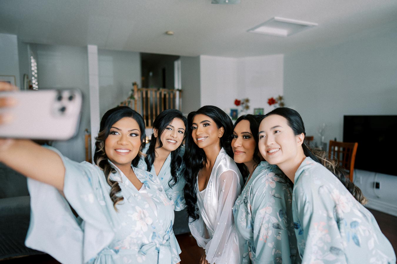 Group of smiling women in floral robes taking a selfie, celebrating a special occasion in a cozy living room.