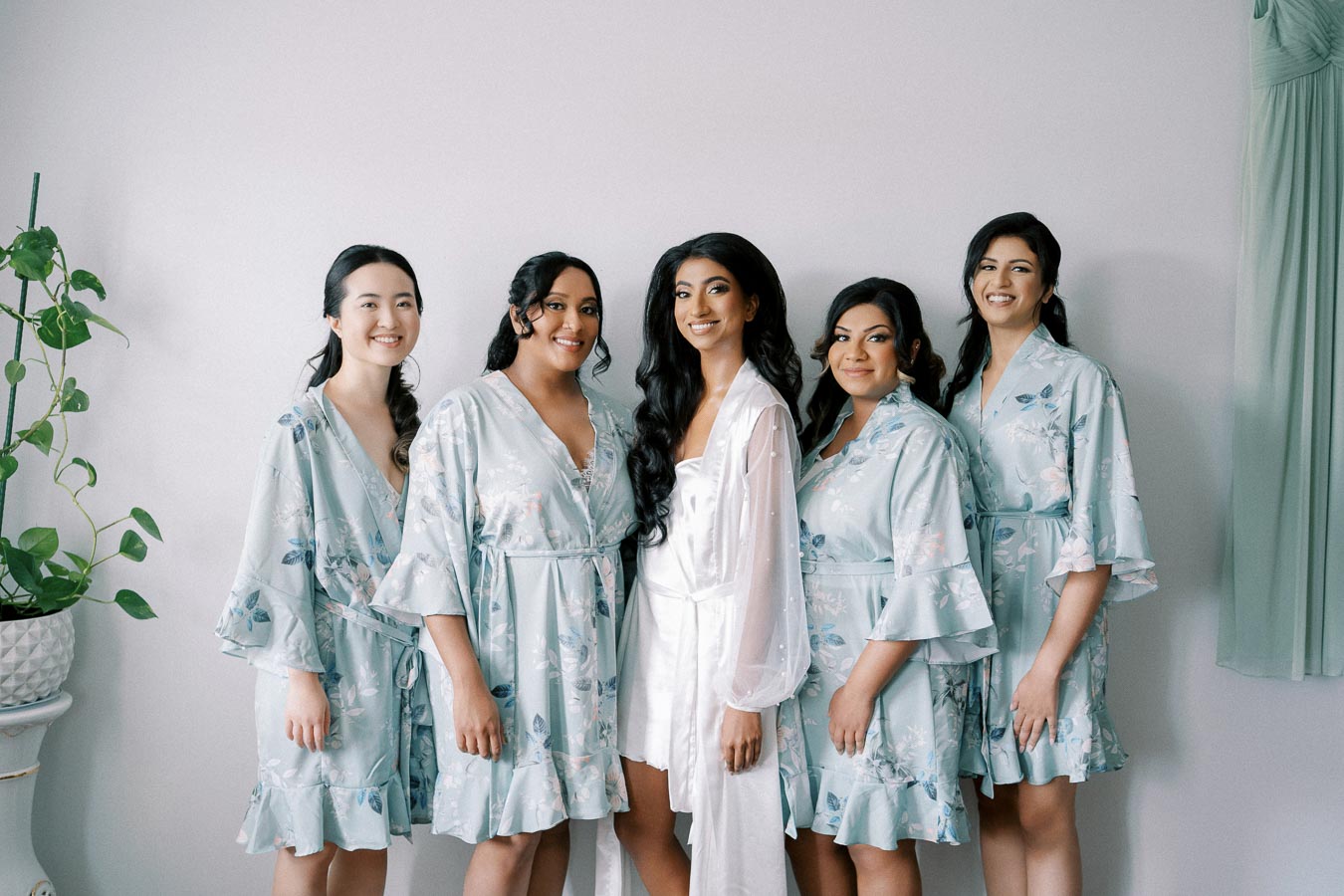 Five women in matching light blue floral robes, standing together in a bright room, smiling at the camera.