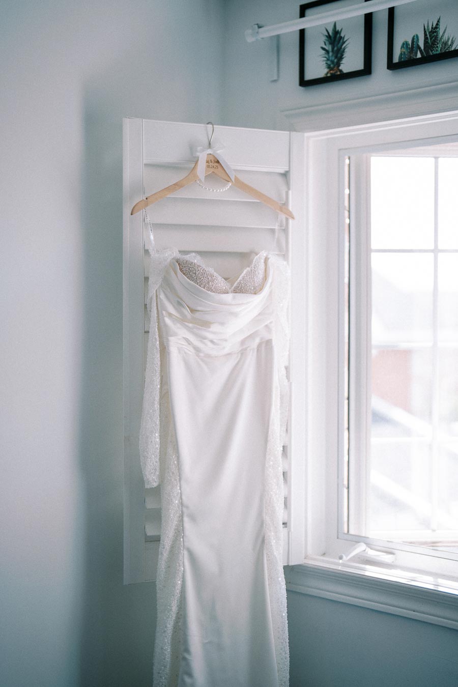 Elegant white wedding dress with lace sleeves hanging by a sunny window, capturing soft natural light, perfect for a bridal fashion inspiration.