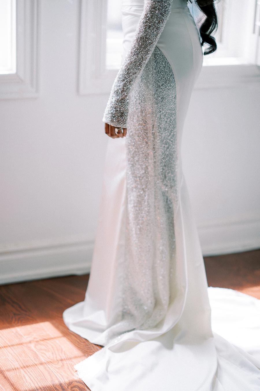 Elegant white and silver bridal gown with sparkling details, featuring long sleeves and a flowing train, captured in natural light.