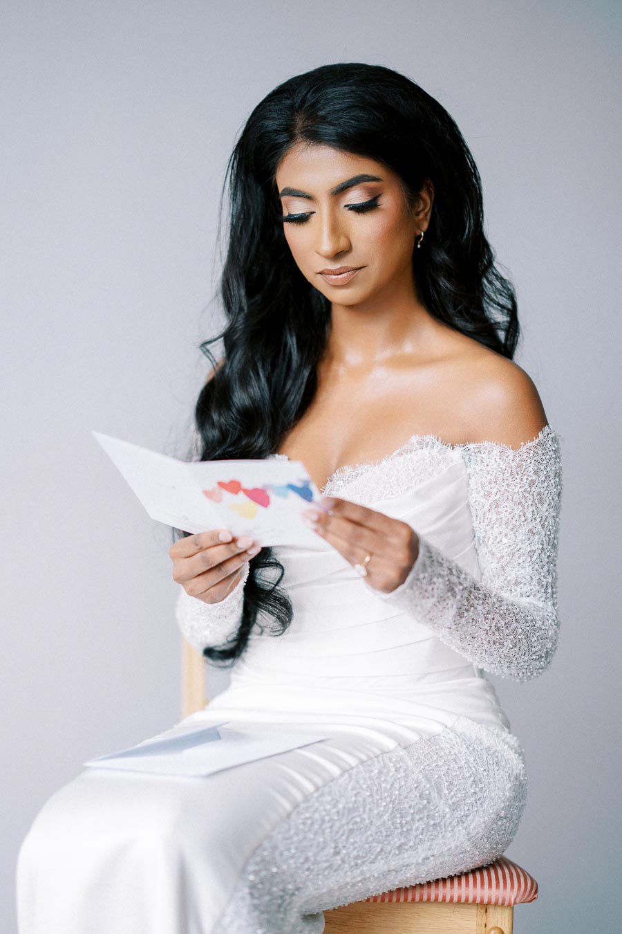 Bride in elegant white wedding dress reading a heartfelt letter, showcasing intricate lace details and beautifully styled long hair. Perfect for wedding inspiration and bridal fashion.