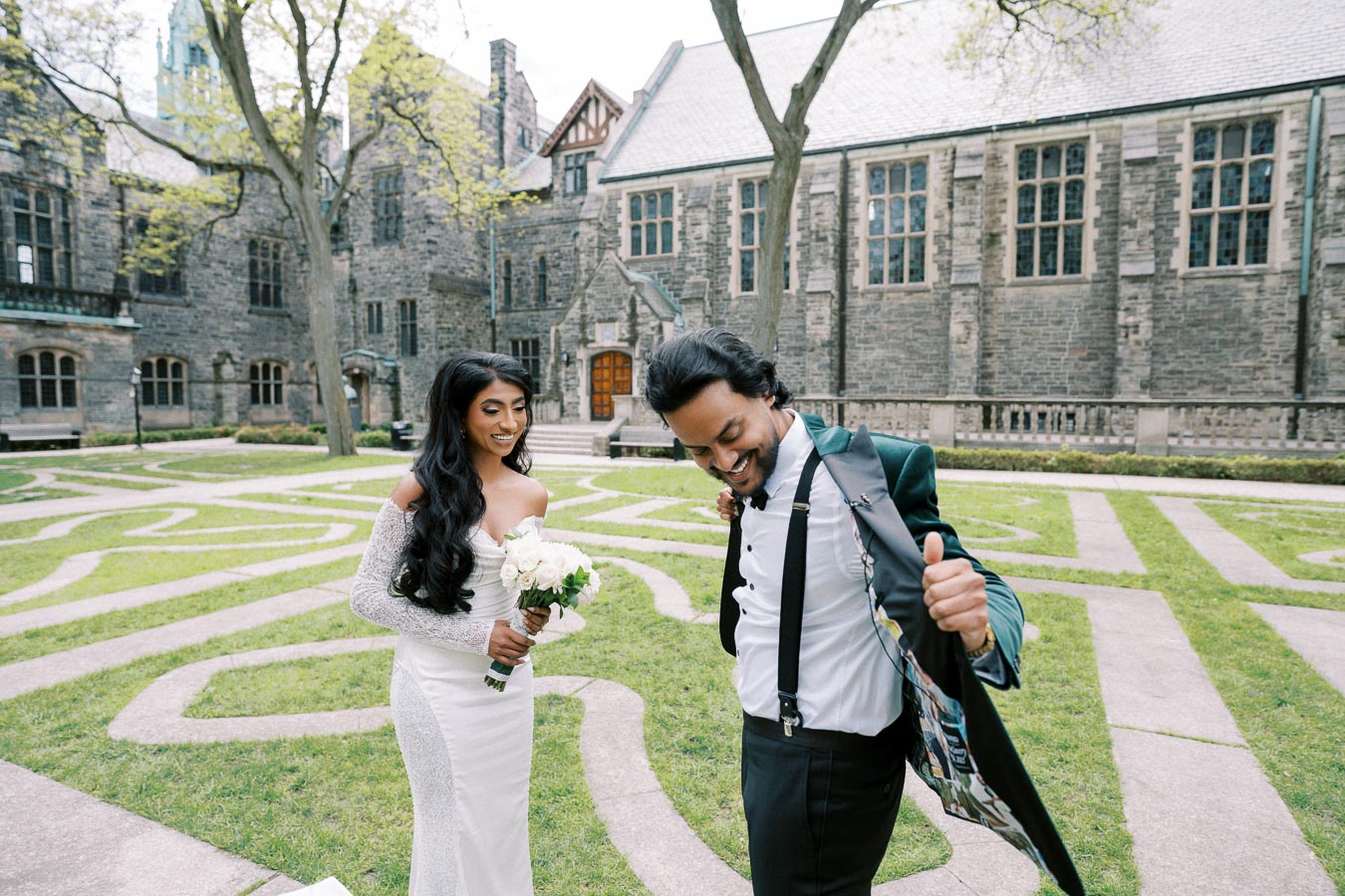A happy couple enjoying their wedding day in a picturesque courtyard with an elegant stone building in the background. The bride is wearing a stunning white dress and holding a bouquet of white flowers, while the groom is adjusting his suit jacket with a joyful expression.