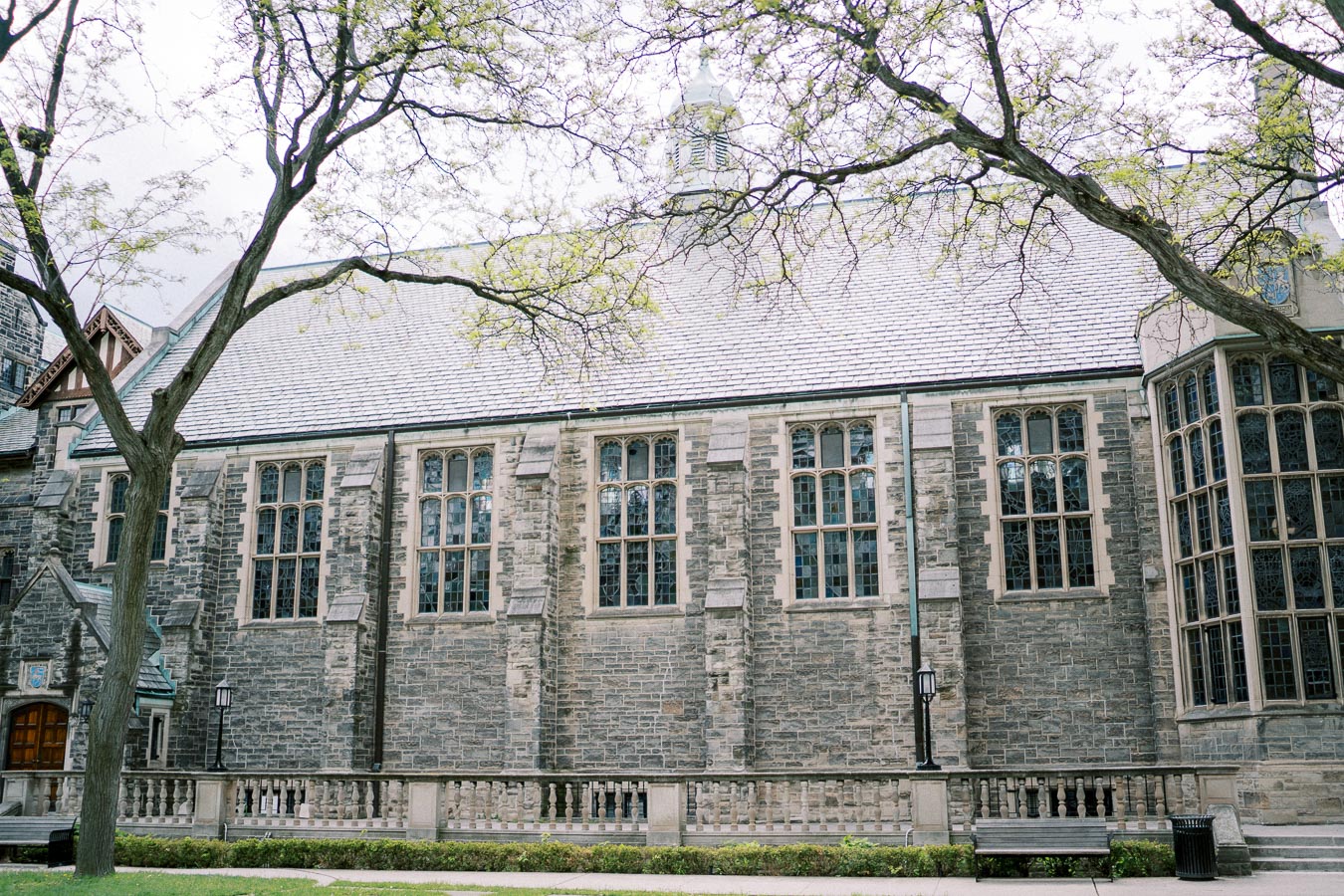 A historic stone building with large, arched windows and trees framing the view, showcasing classic architectural design.