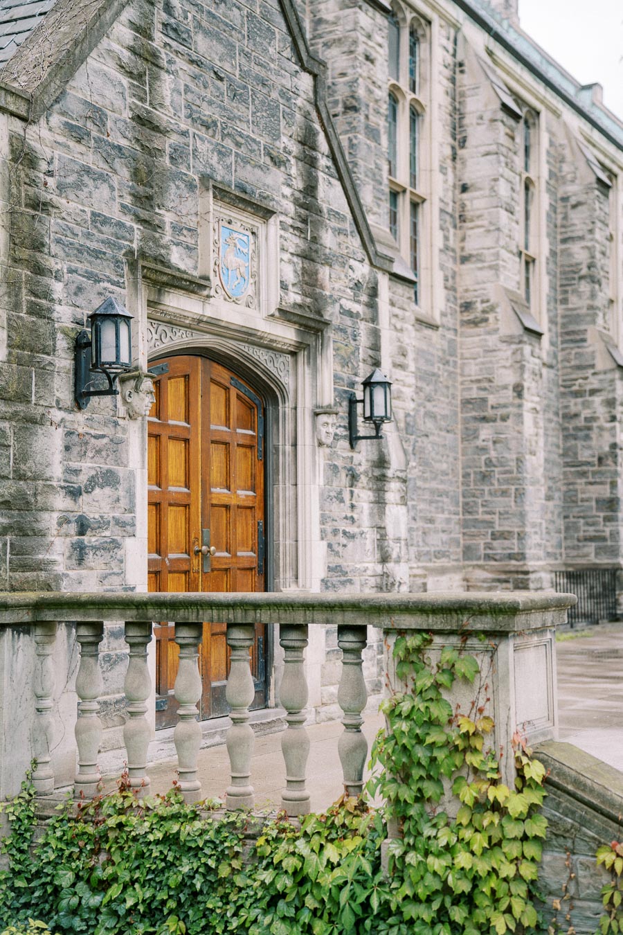 Historic stone building facade with a wooden arched door, ivy-covered stone railing, and architectural details, symbolizing classic architecture and heritage.
