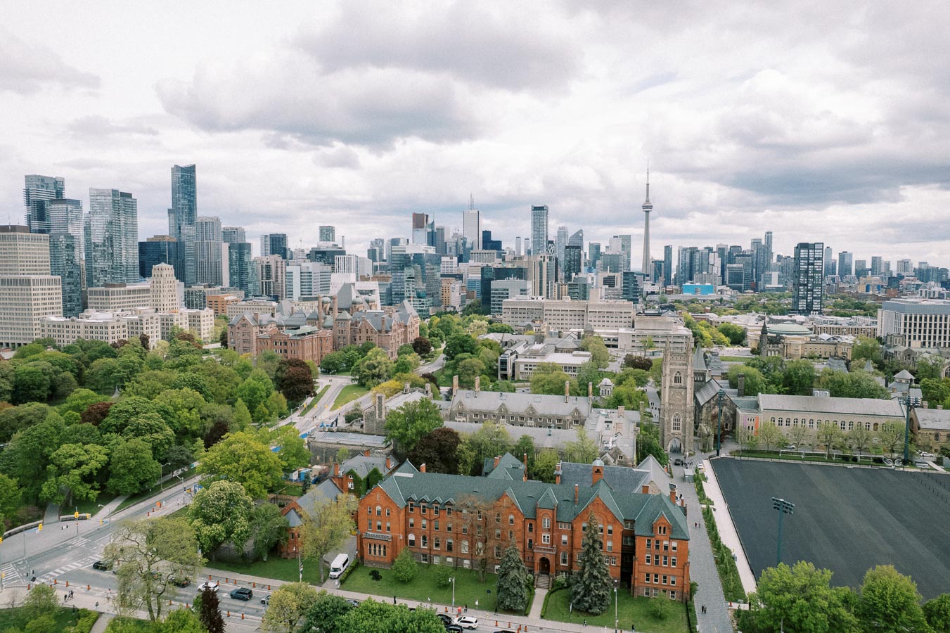 Aerial view of a cityscape featuring modern skyscrapers, historic buildings, and lush green parks under a cloudy sky, showcasing the blend of urban and natural elements.