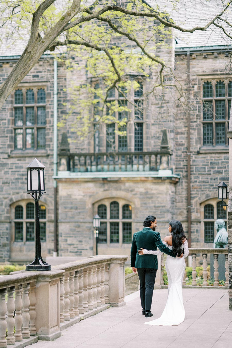 Elegant couple walking arm-in-arm along a historic stone building, showcasing romantic architecture and graceful surroundings.