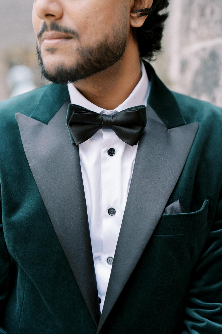 A man wearing an elegant dark green velvet tuxedo jacket with a black bow tie, highlighting formal fashion and style.