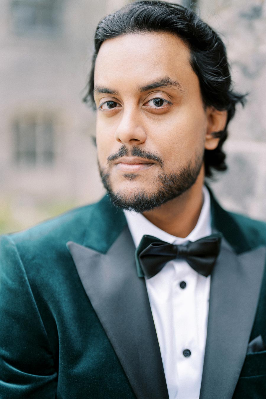 Portrait of a man in a formal suit with a bow tie, looking confidently at the camera with a blurred outdoor background. Perfect for professional profile or business attire content.
