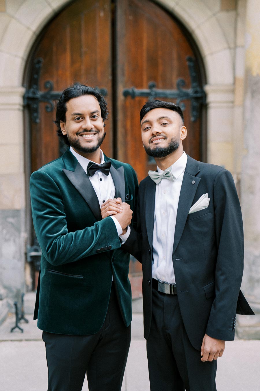 Two men in formal attire smiling and shaking hands in front of a wooden door.