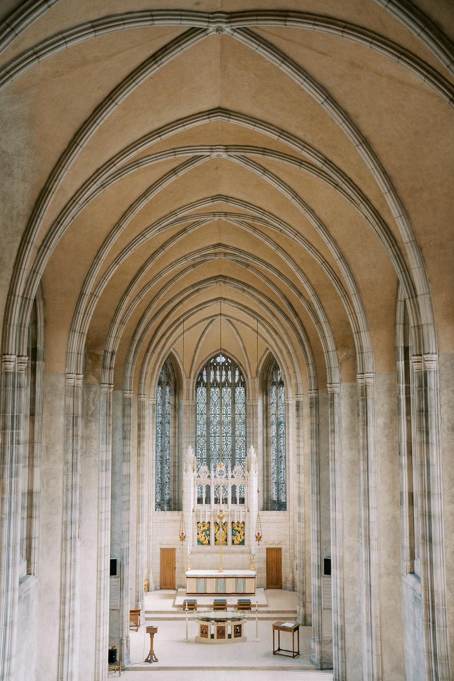 Gothic cathedral interior with vaulted arches and ornate altar, featuring intricate stained glass windows and stone columns.