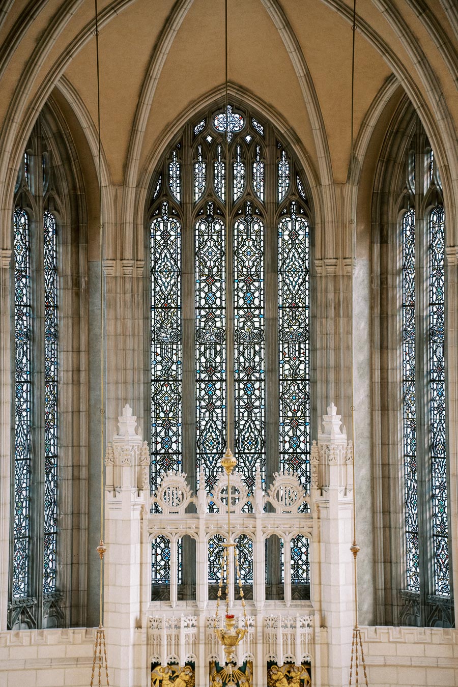 Interior view of a cathedral featuring ornate stained glass windows and intricate gothic architecture with pointed arches and decorative stonework.