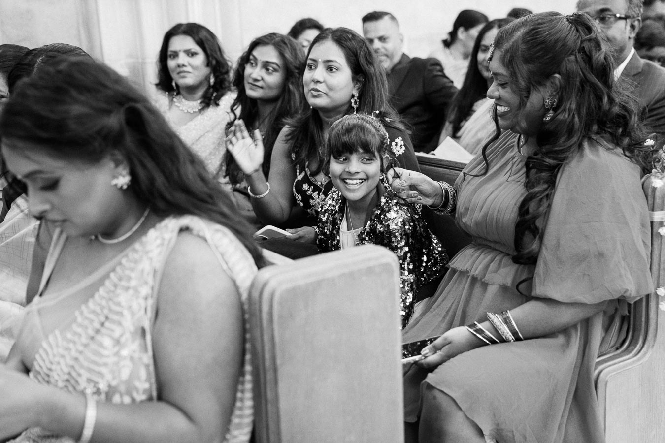 Group of people enjoying a formal event in an indoor setting, featuring elegantly dressed women and a smiling child in the center, capturing a joyful and festive atmosphere.