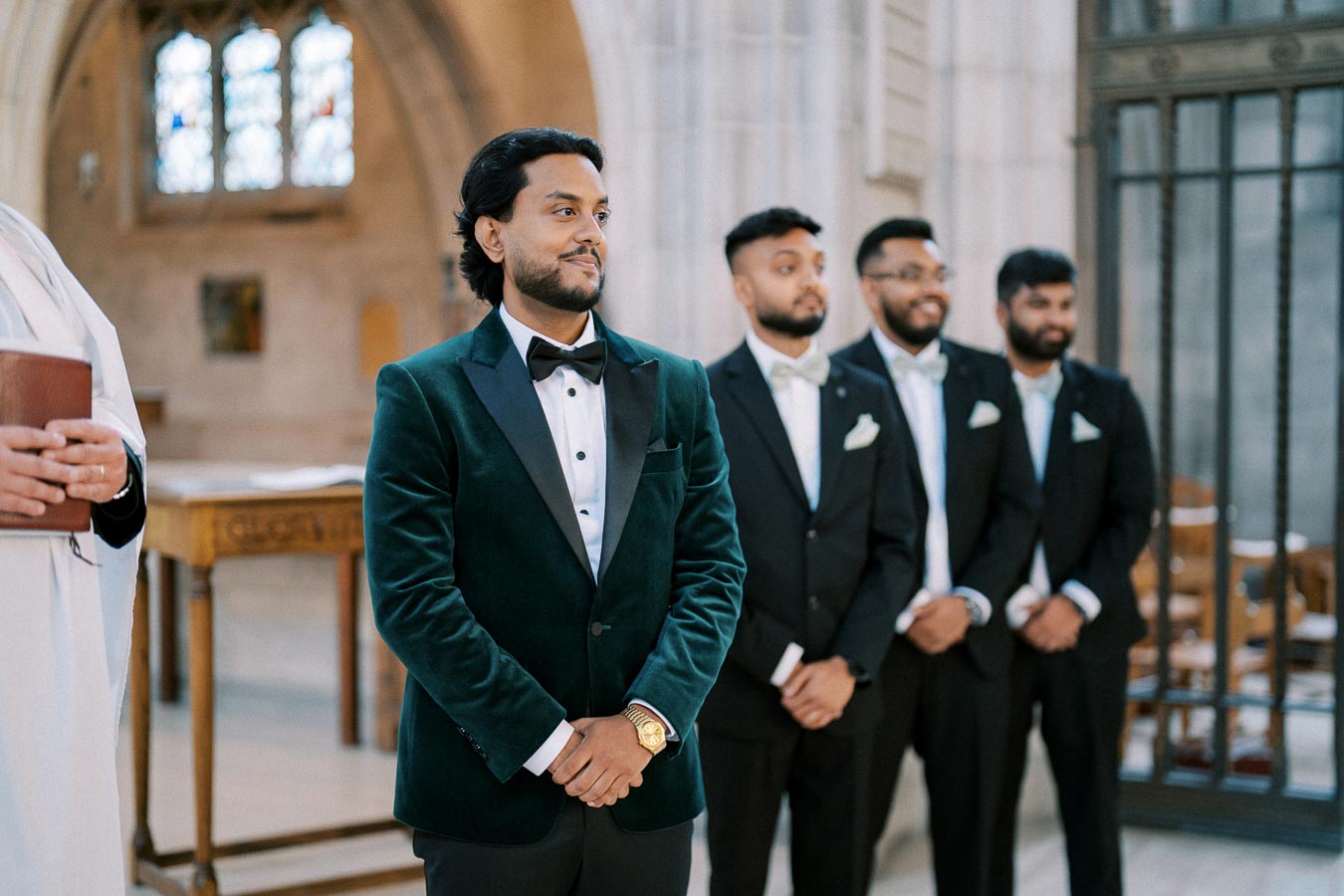 Groom in a green velvet tuxedo with groomsmen standing in a church, preparing for a wedding ceremony.