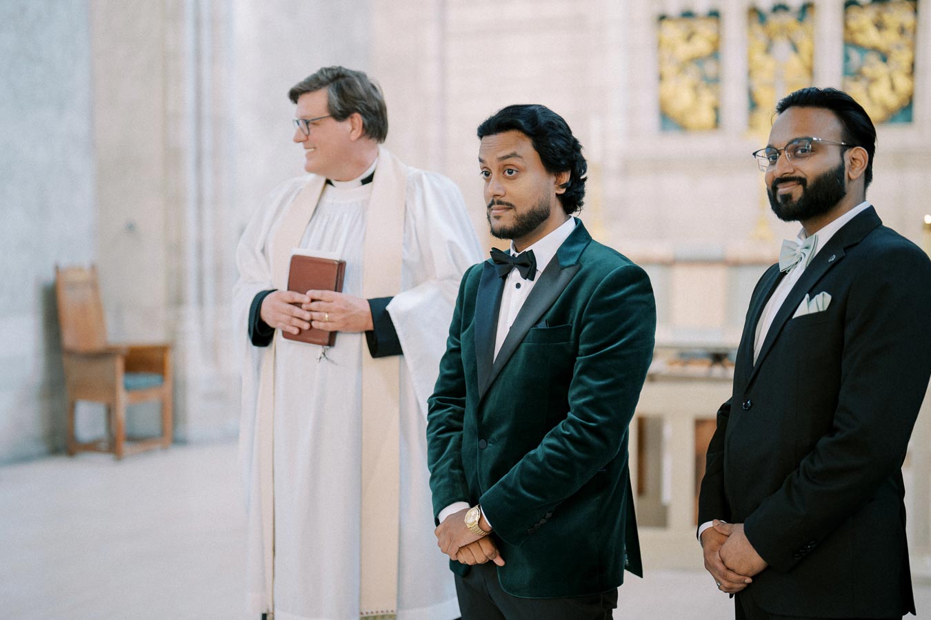 Groom in a green velvet tuxedo with best man and officiant at a wedding ceremony in a church setting.