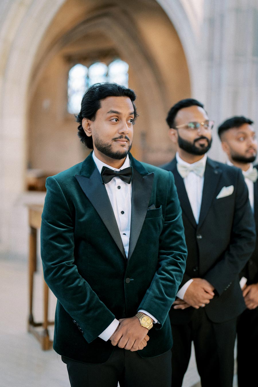 Groom in velvet tuxedo with groomsmen at elegant wedding ceremony inside a church