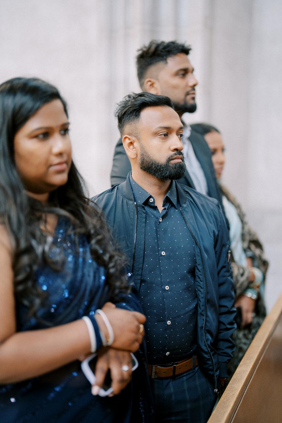 A group of people attentively listening during a formal indoor gathering, with two individuals in focus wearing smart attire.