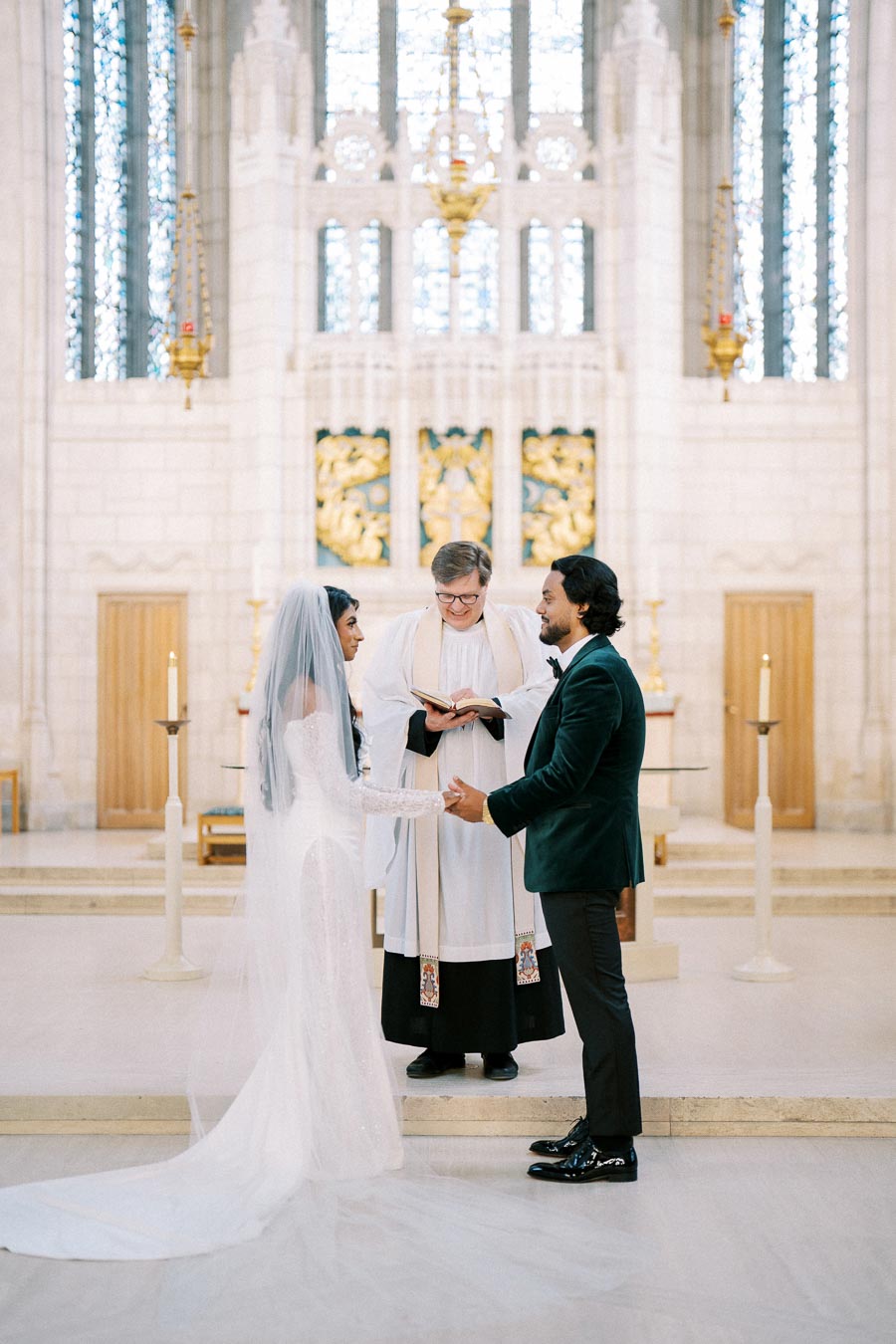 A bride and groom exchange vows during a wedding ceremony in a beautifully adorned church, with an officiant guiding them.