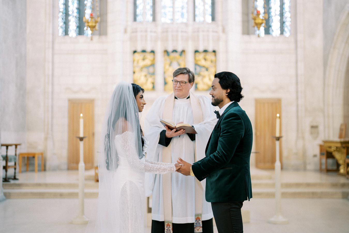 A couple exchanging vows in a church wedding ceremony, with a priest officiating and candles lit in the background.