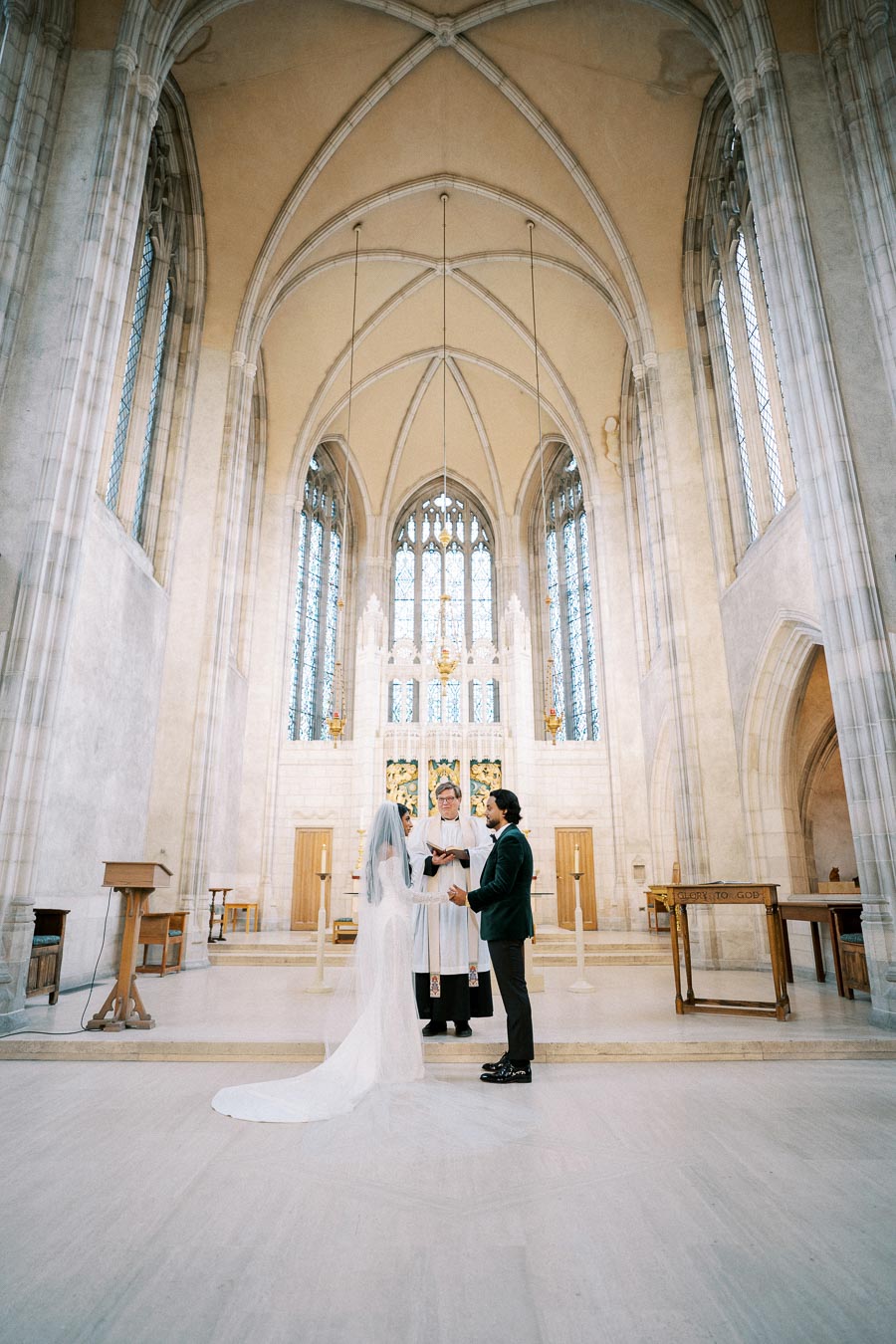 A couple exchanging vows during a wedding ceremony in a grand cathedral with stunning high ceilings and stained glass windows.