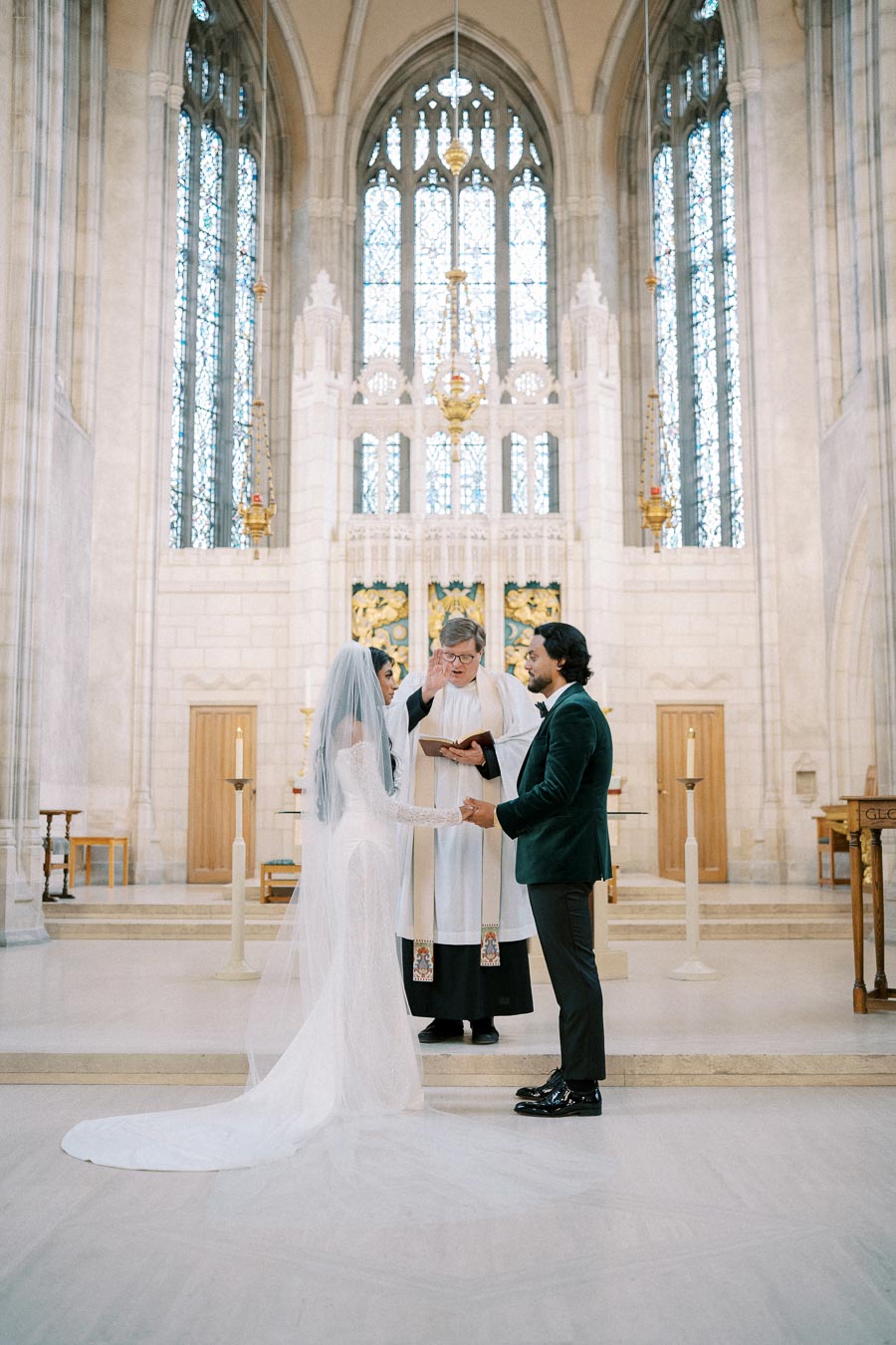 Ceremony in a grand church with a bride and groom exchanging vows in front of a priest, beautiful stained glass windows and intricate architecture in the background.