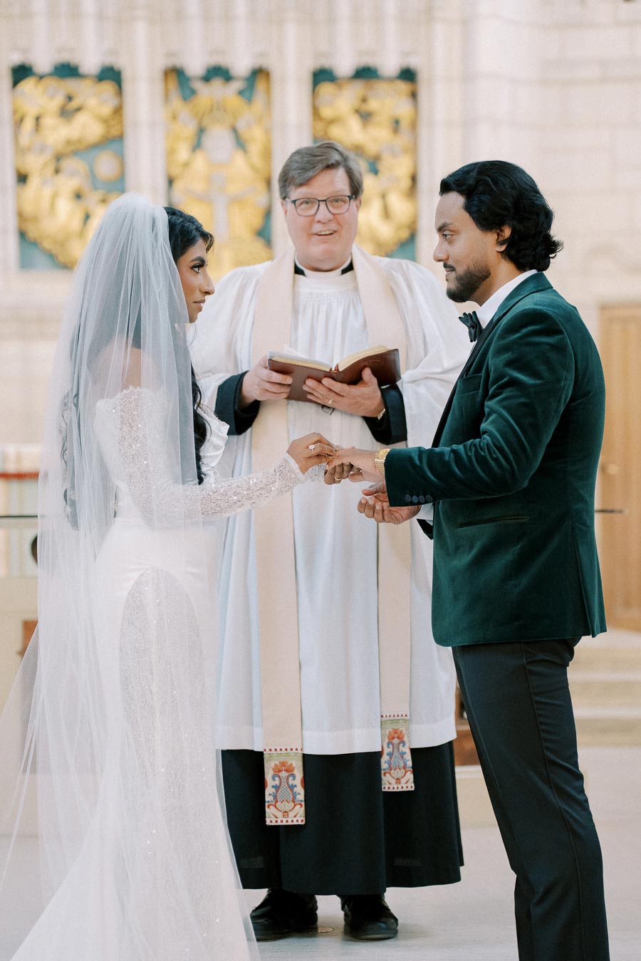 Bride and groom exchanging vows in a church ceremony, with the officiant holding a book behind them.