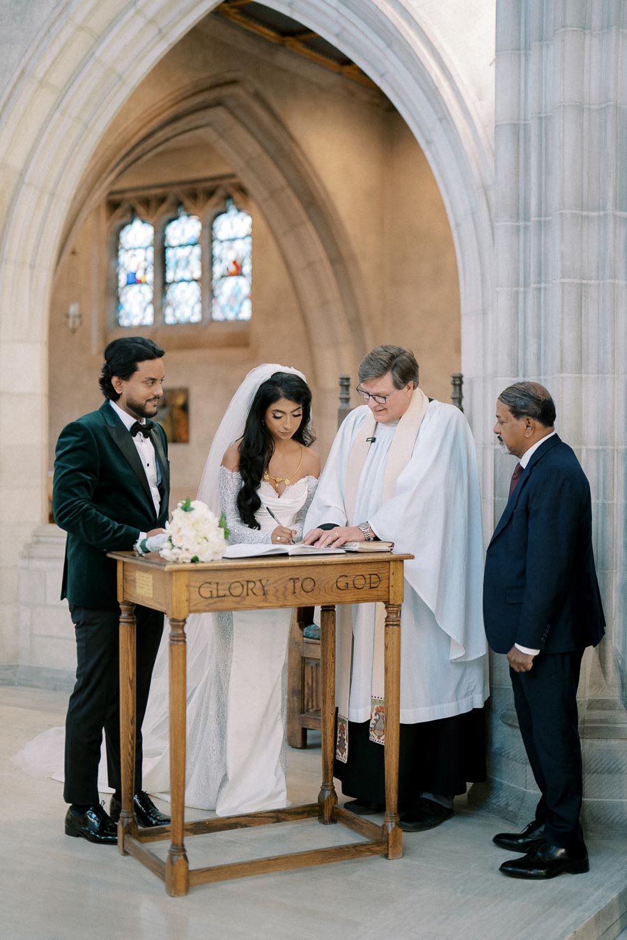 Bride and groom signing a marriage certificate in a church, with an officiant and witnesses nearby.