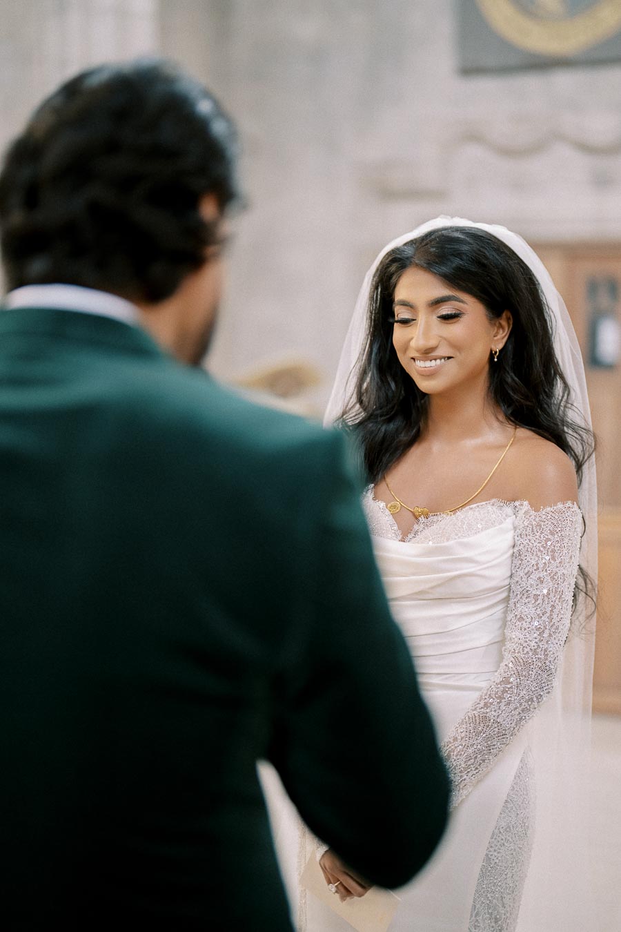 Bride in elegant lace wedding dress smiling during wedding ceremony.