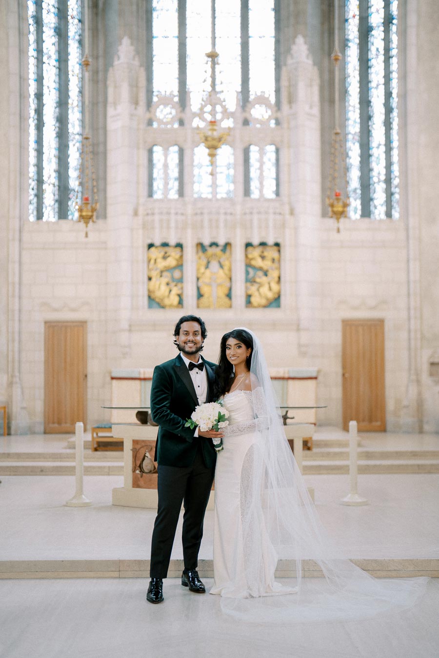 Elegant wedding couple poses inside a grand church, with intricate stained glass windows and detailed altar backdrop, capturing a timeless and romantic moment.