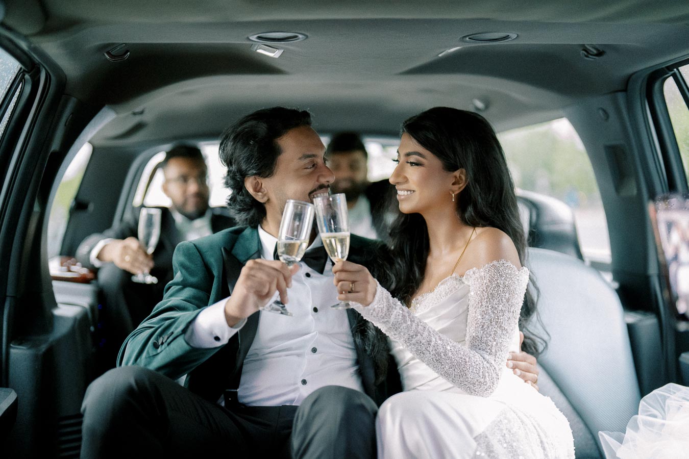 Smiling newlyweds toasting with champagne in a limousine, surrounded by friends, after their wedding ceremony