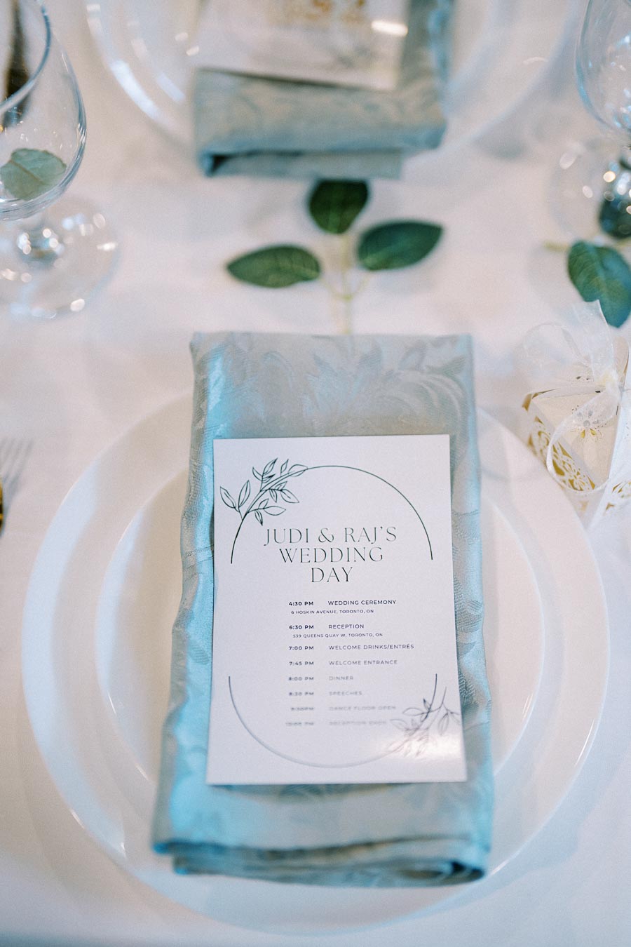 Elegant wedding table setting with a blue napkin and a wedding itinerary card detailing the schedule for a ceremony and reception.