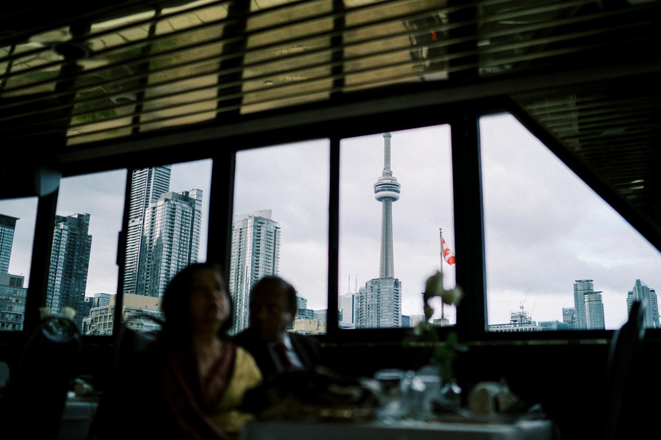 Toronto skyline featuring the CN Tower viewed from inside a restaurant, including an out-of-focus couple in the foreground.