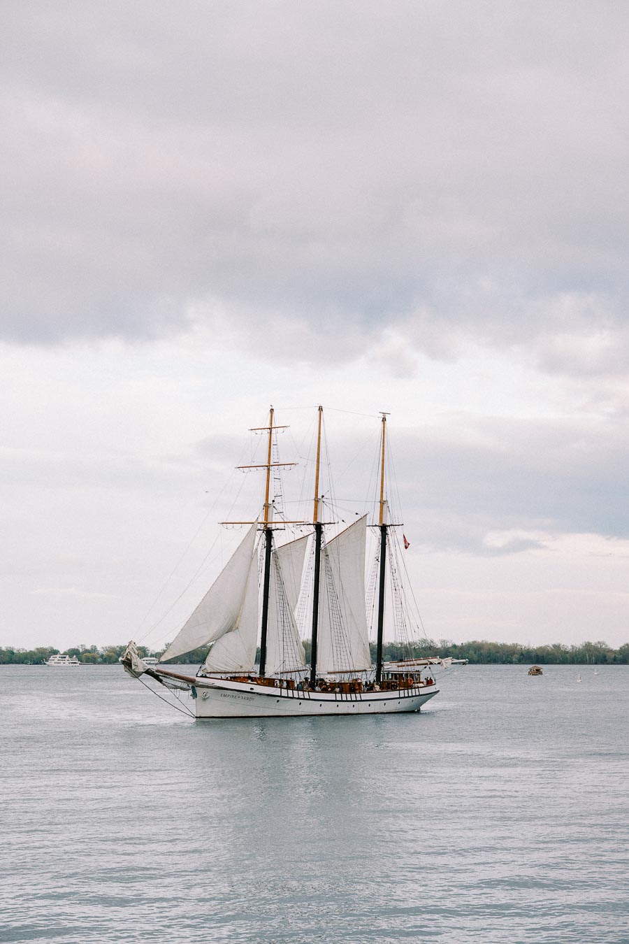 Sailing ship with white sails on calm water under cloudy sky
