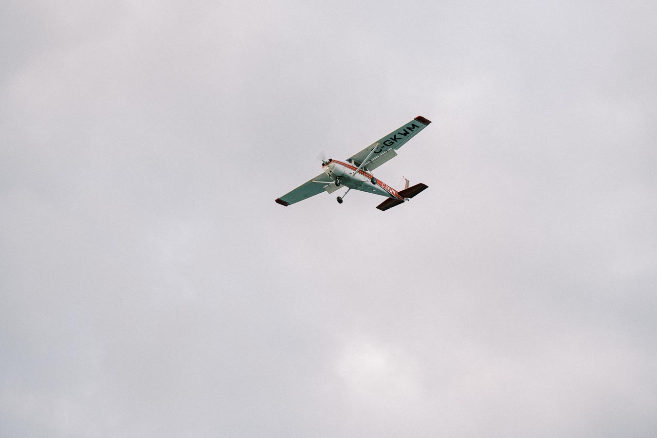 Small white and red airplane flying against a cloudy sky, showcasing light aircraft in flight.