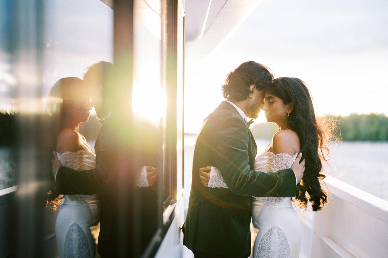 A couple embracing on a boat at sunset, with the sun lighting up the scene and reflecting on the glass.