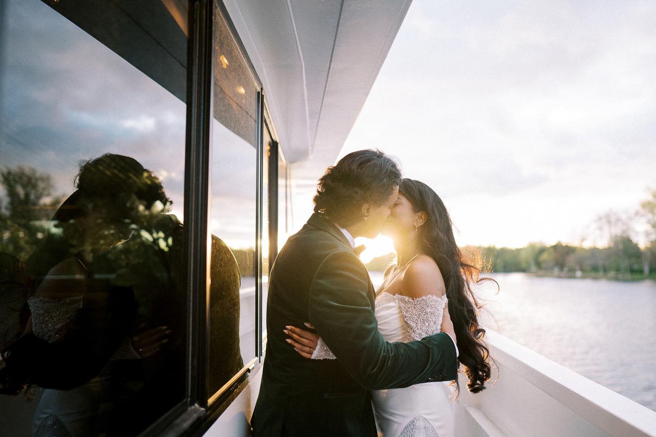 A romantic couple sharing a kiss on a boat at sunset, with reflections on the window and a serene lake in the background.