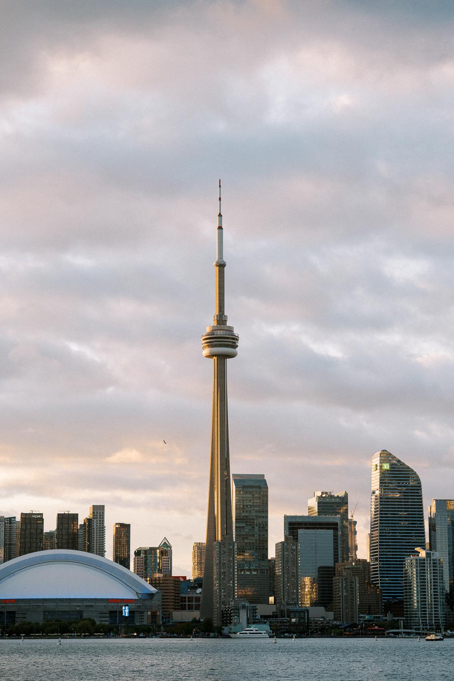 Skyline of Toronto with the CN Tower at sunset, featuring modern skyscrapers and waterfront reflections.