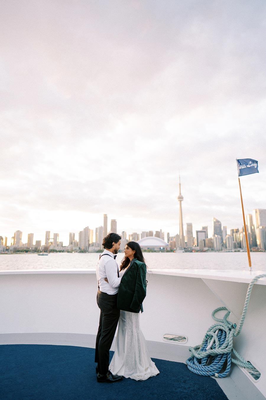 A couple embracing on a boat with the Toronto skyline in the background at sunset, featuring the CN Tower and Lake Ontario.