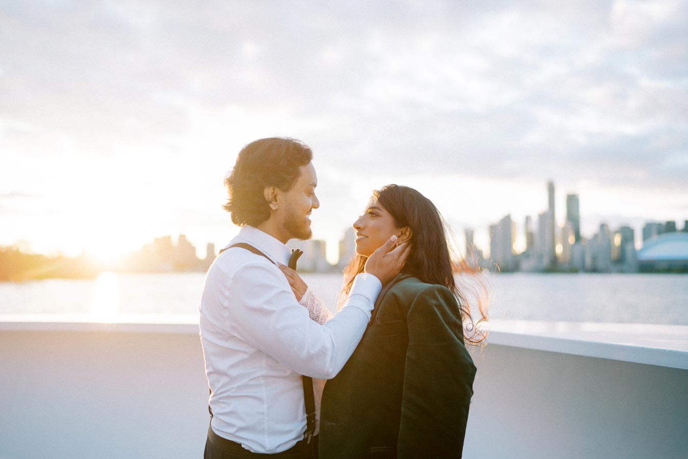 A couple embracing on a boat at sunset with a city skyline in the background.