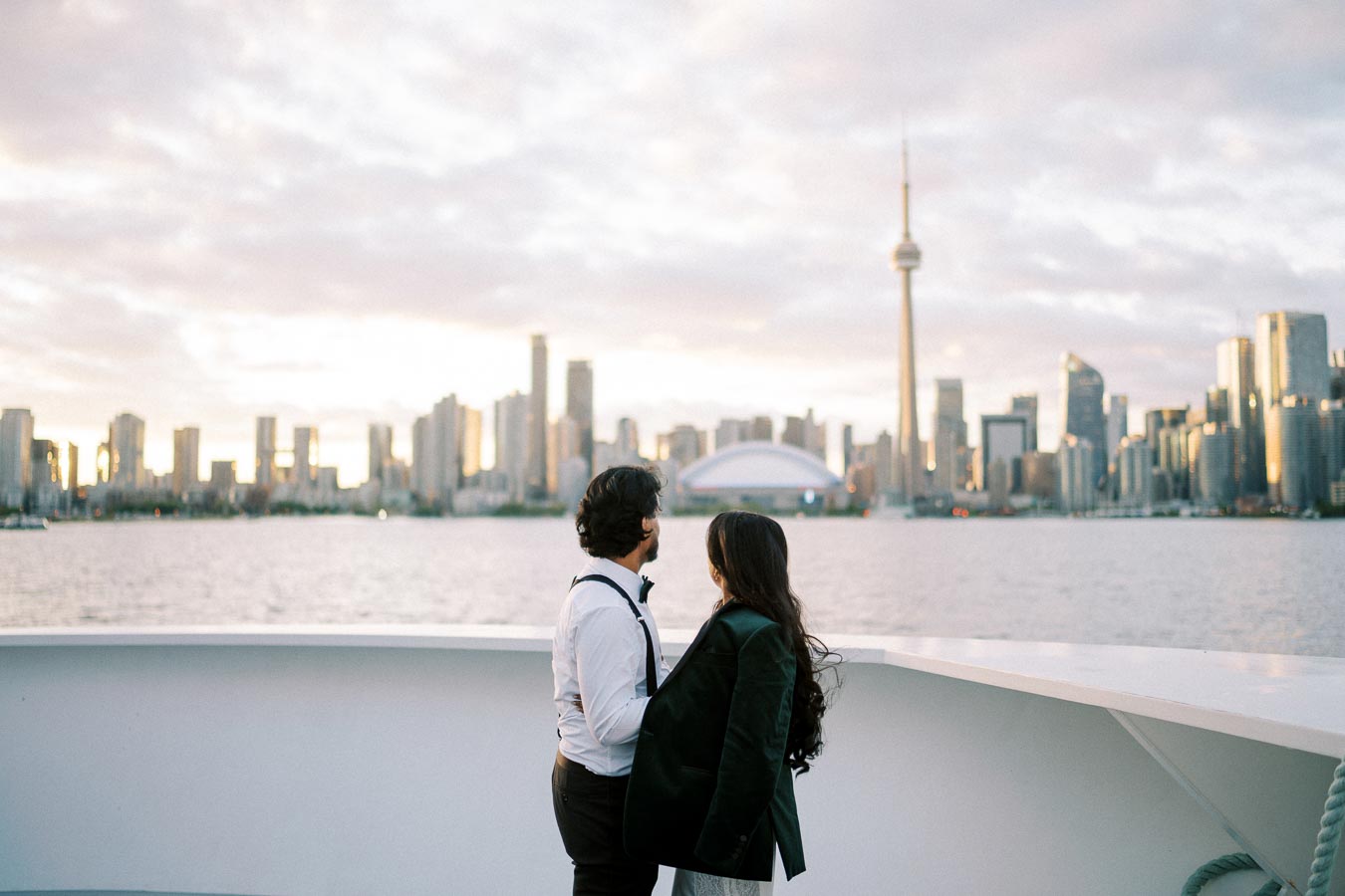 A couple embraces on a boat, overlooking the Toronto skyline with the CN Tower at sunset.