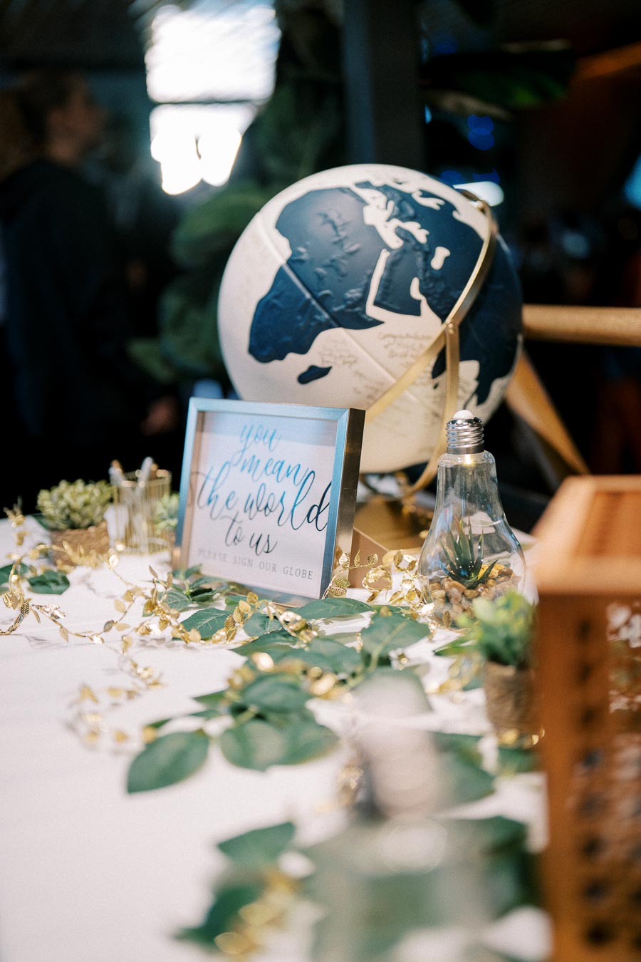 Table with decorative globe, framed sign reading You mean the world to us, greenery, and string lights, creating an inviting atmosphere for guests.