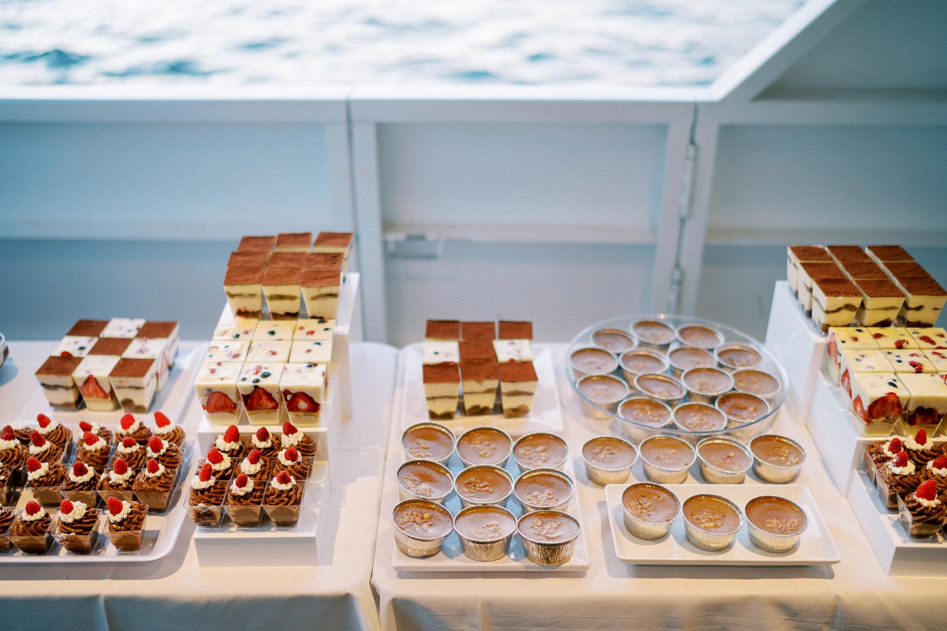 Assorted gourmet desserts displayed on a table aboard a ship, featuring tiramisu, layered fruit cake, chocolate mousse, and crème brûlée, providing a delectable variety for catering or special events.