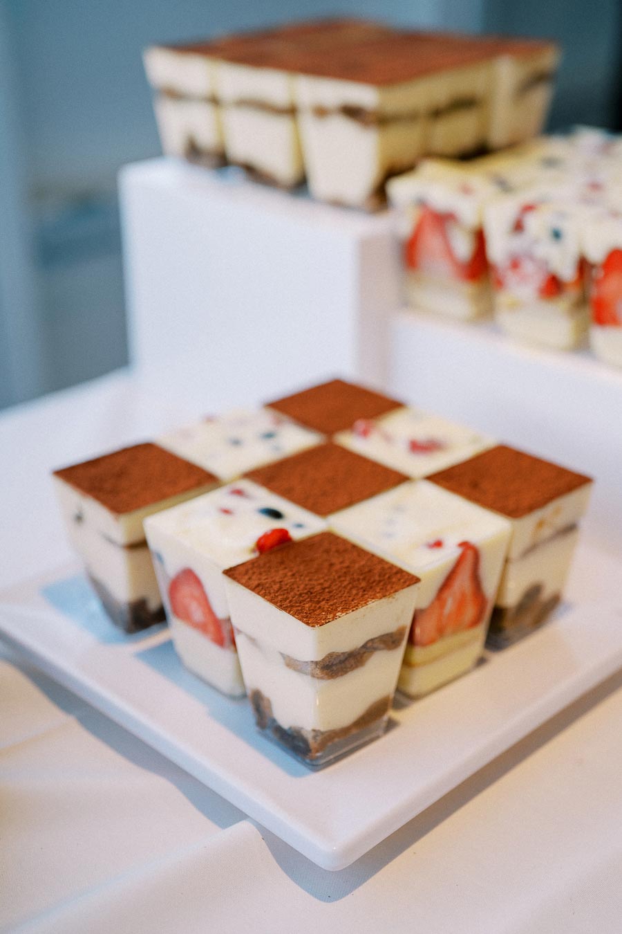Delicious layered dessert cups featuring creamy tiramisu squares with cocoa topping and fresh strawberry pieces, elegantly displayed on a white plate for a tempting treat.