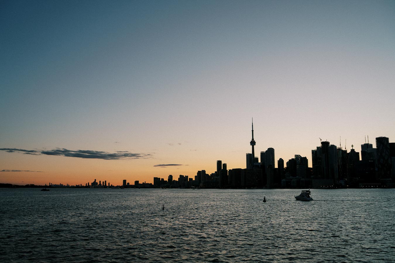 Sunset view of Toronto skyline with CN Tower and Lake Ontario in foreground.