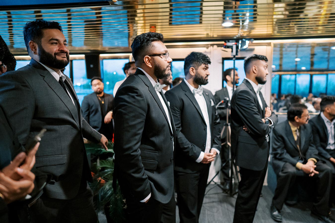 Group of men in formal suits at a business event, attentively listening to a speaker in a modern conference setting.