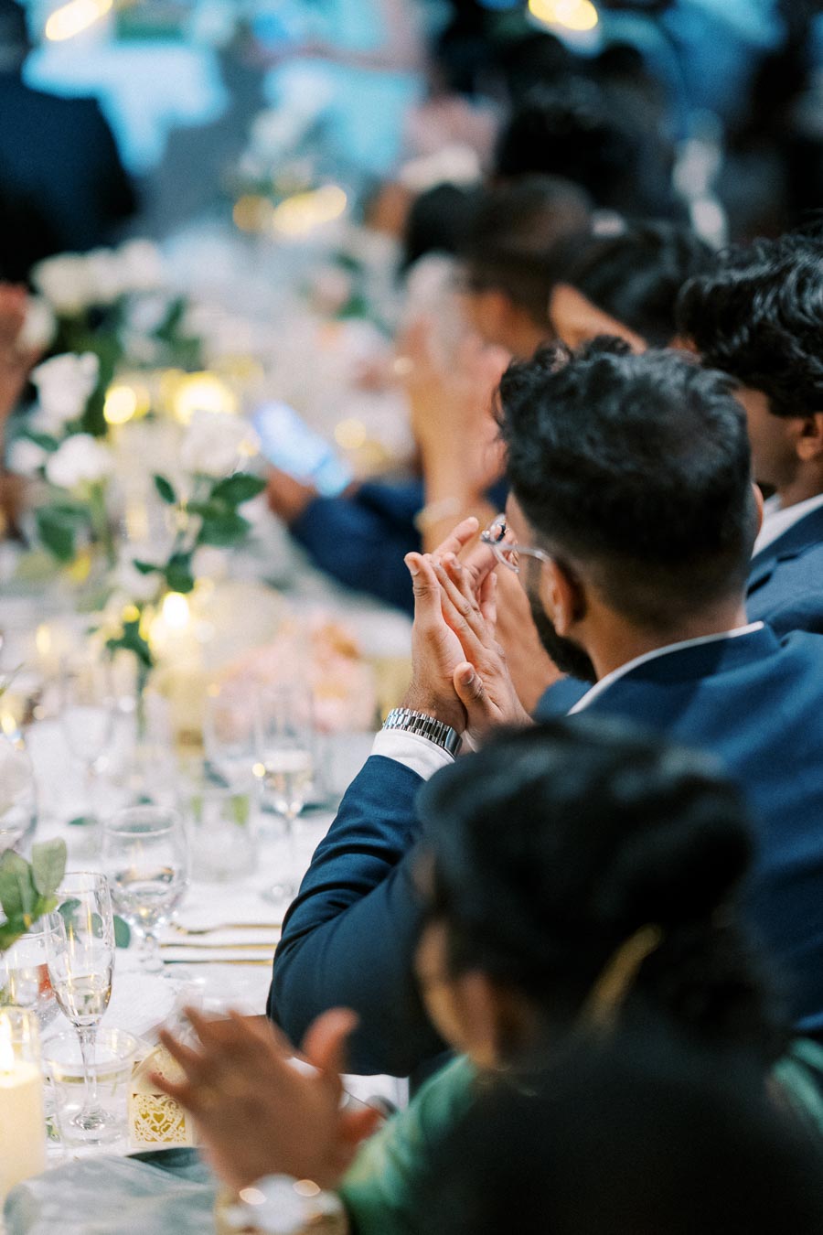 Guests clapping at a formal event, seated at a beautifully decorated table with flowers and candles.