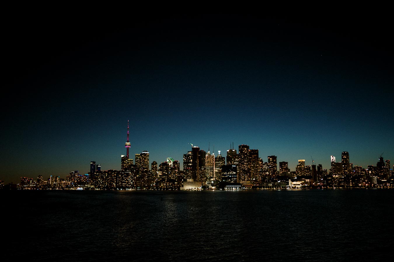 Panoramic night view of illuminated Toronto city skyline with CN Tower and waterfront reflections, Ontario, Canada.
