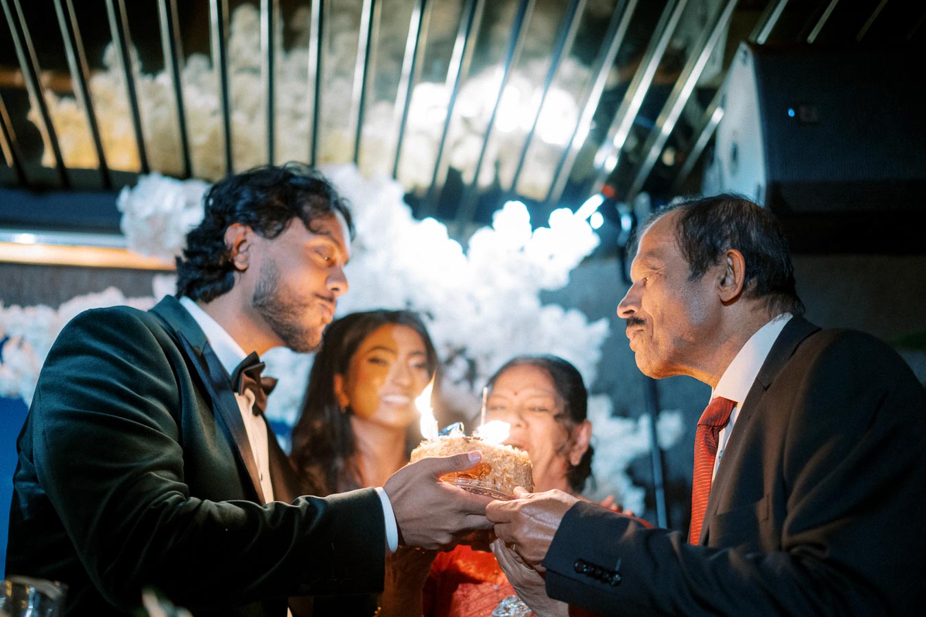A joyful family celebration with four people gathered around a cake with lit candles, in a warmly lit setting, capturing a moment of togetherness.