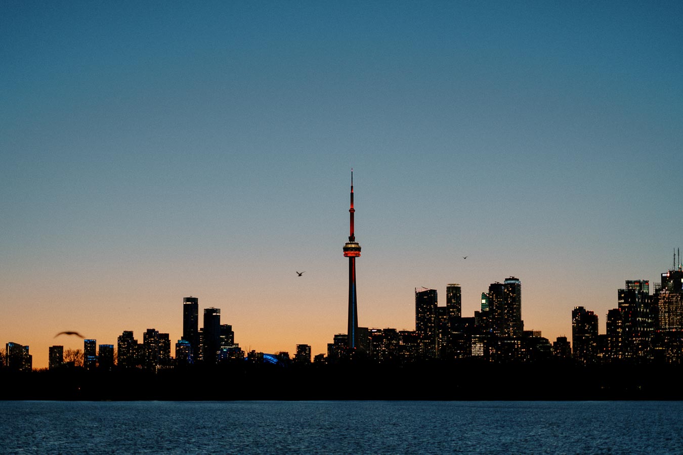 Sunset skyline of Toronto with CN Tower silhouette over Lake Ontario.